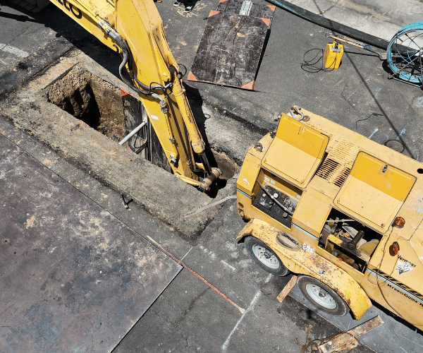 A large yellow construction vehicle with a crane arm parked on a concrete road.